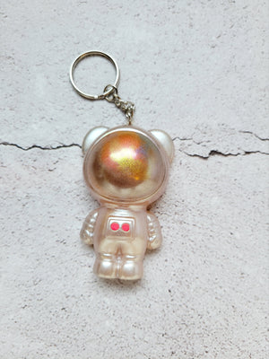 Astronaut bear in pearl space suit with two red buttons. the helmet has color shifting colors to look like a reflected nebula. It has a silver hoop and chain. Top view