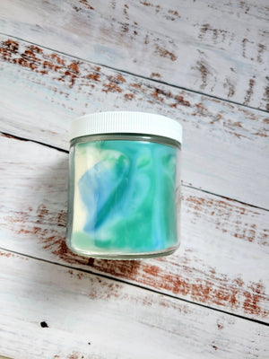 A 12oz marbled candle laying on its side to show the blue and green swirled colors. It has a white lid and glass jar. It's name is Star Wars: Alderaan. It's scent notes include, pine, rose, and red wine.