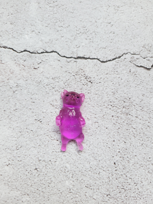 A small corgi figure sleeping on its back with black painted eyes and nose. It is a pinkish purple color.