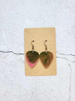 A pair of guitar pick earrings on a cardboard backer card. The hook earrings are antique coloring. The picks are a mix of pink, green, and glitter. 