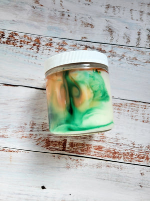 A side view of a 12oz marbled candle to show the yellow and green swirls in the wax. It's in a glass jar with a white lid. This candle is called Wild Magic Surge: Witch's Hut. It's scent profile is spiced honey, mint, tonka. There is a mystery Dungeons and Dragons die inside.