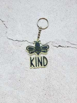 Keychain with a silver hoop. It's yellow with black highlights on the bee and  the words Kind