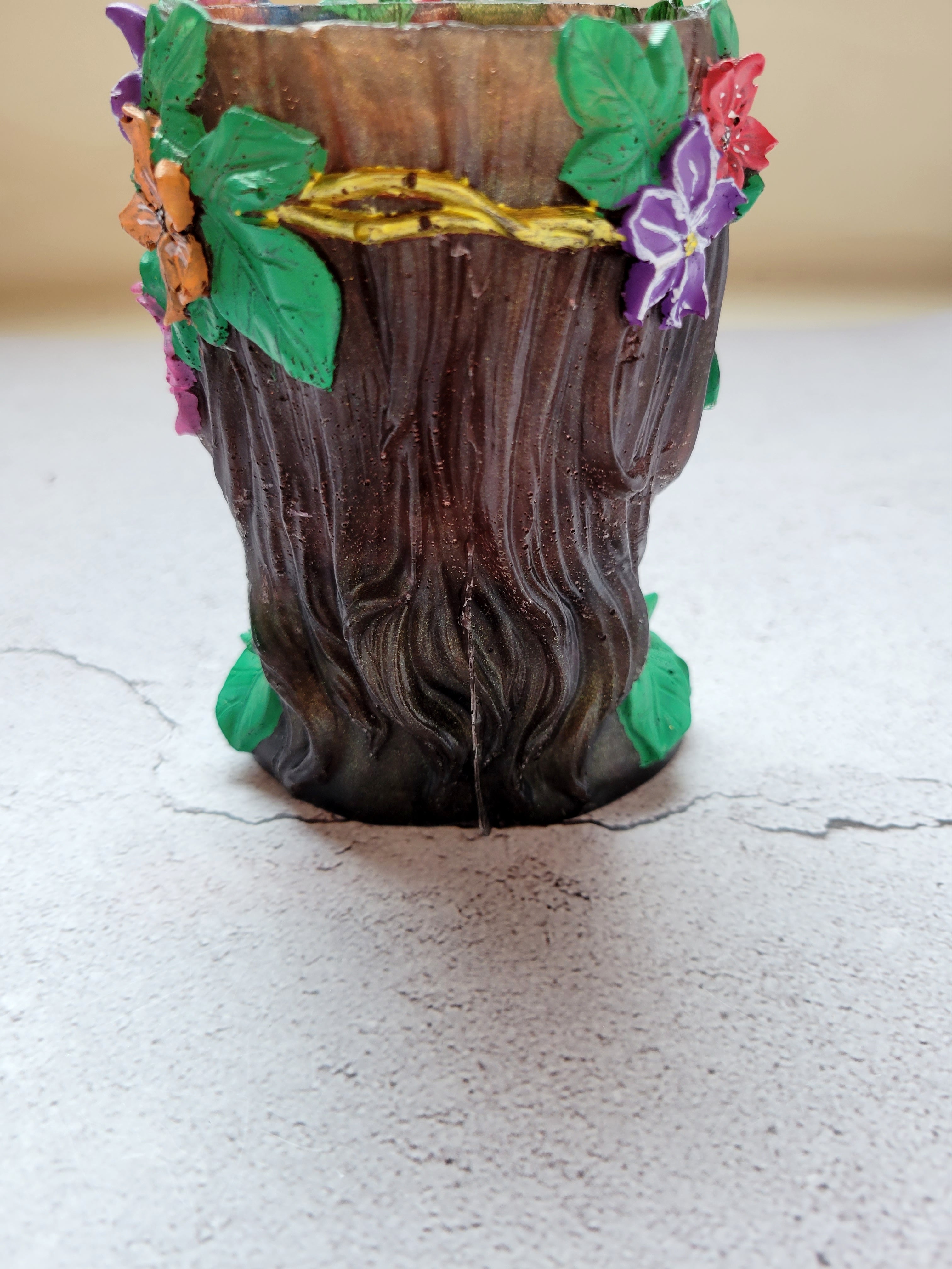 brownish bronze colored resin woman's face with green eyes, green ivy around her neck, a golden stem crown filled with colorful flowers. Back view