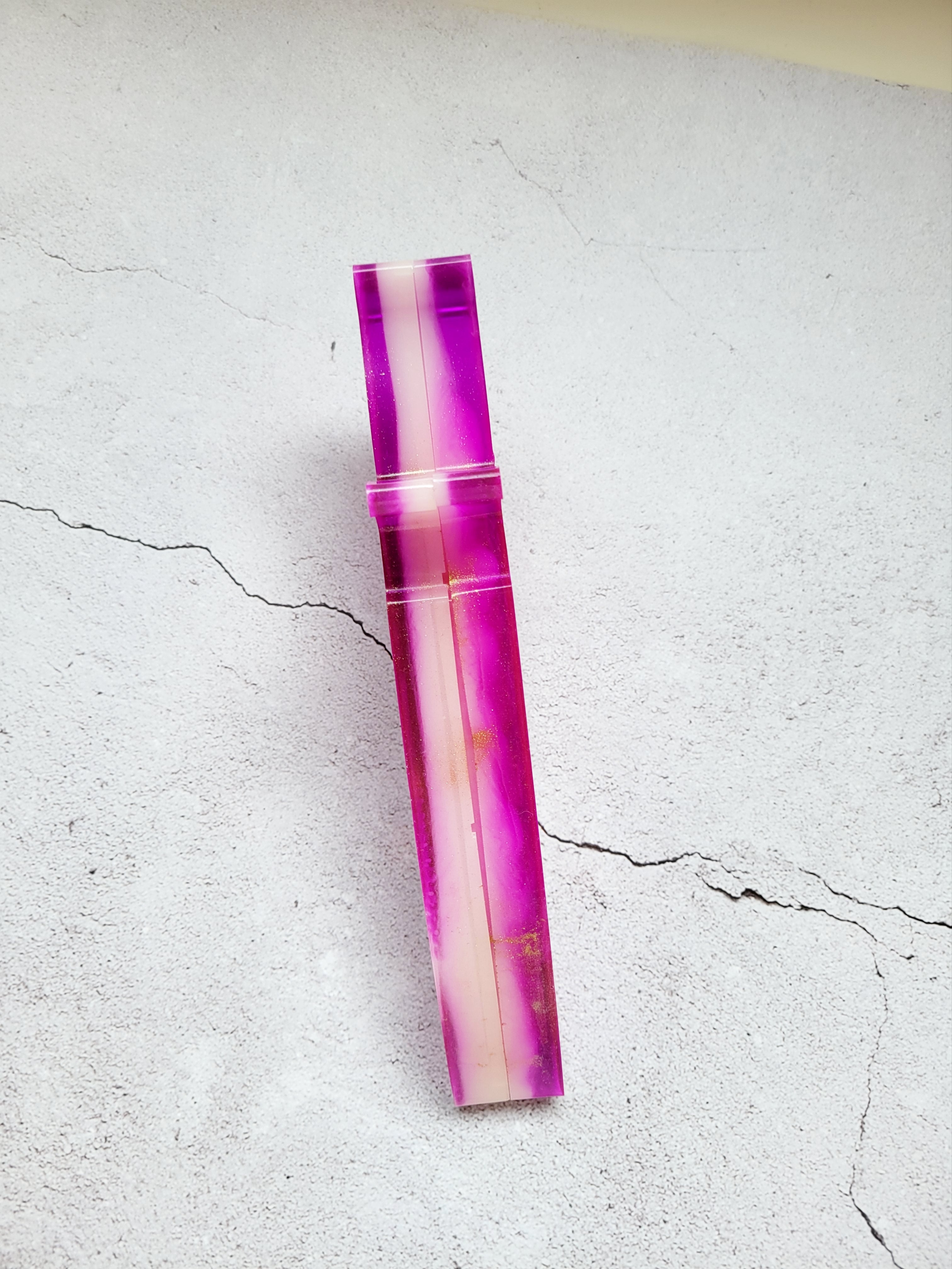 resin dice dagger, closed. It's outside is bright pink, the inside is white with gold spray. Top side view