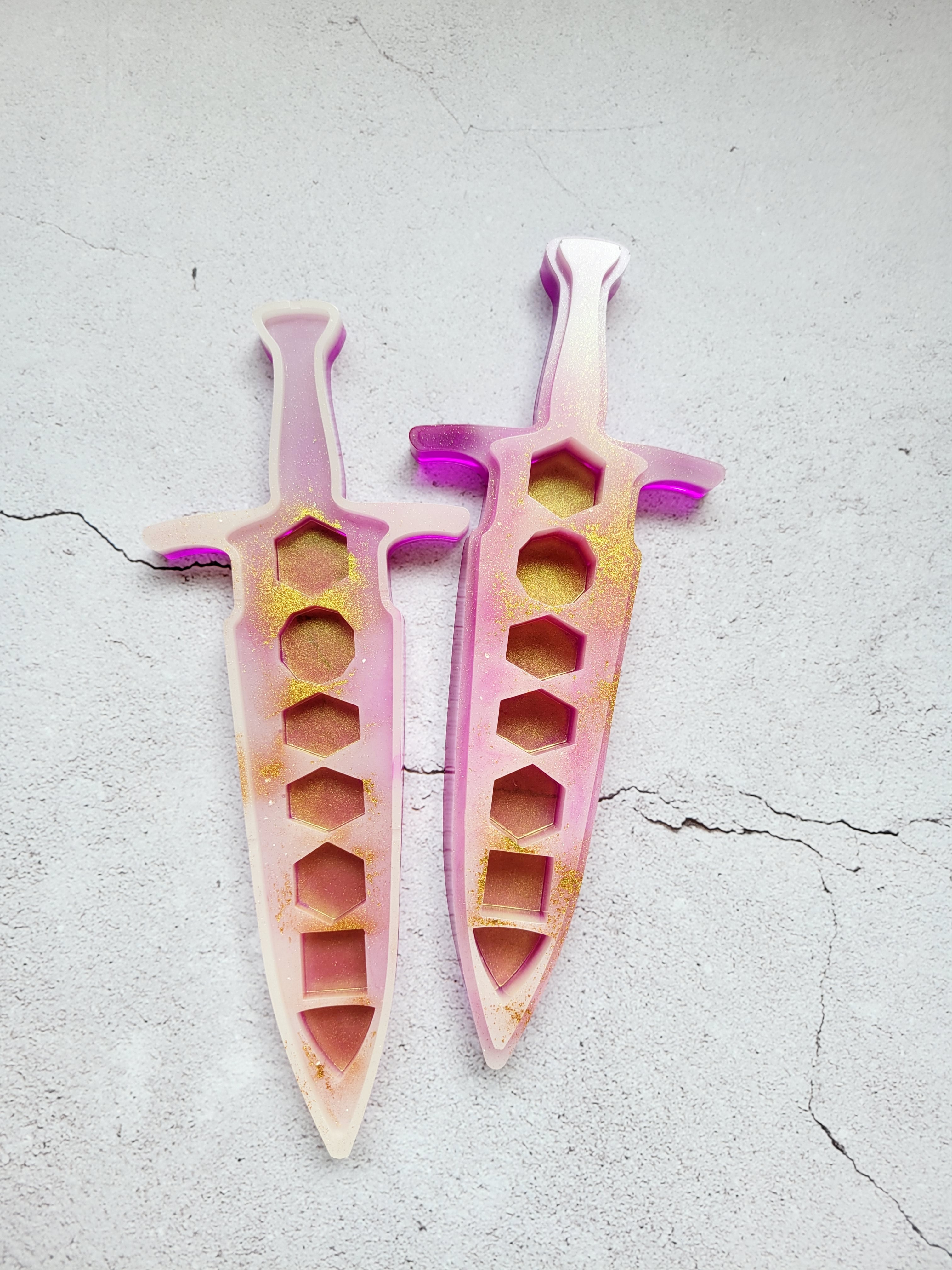 resin dice dagger open. It's outside is bright pink, the inside is white with gold spray. Top view