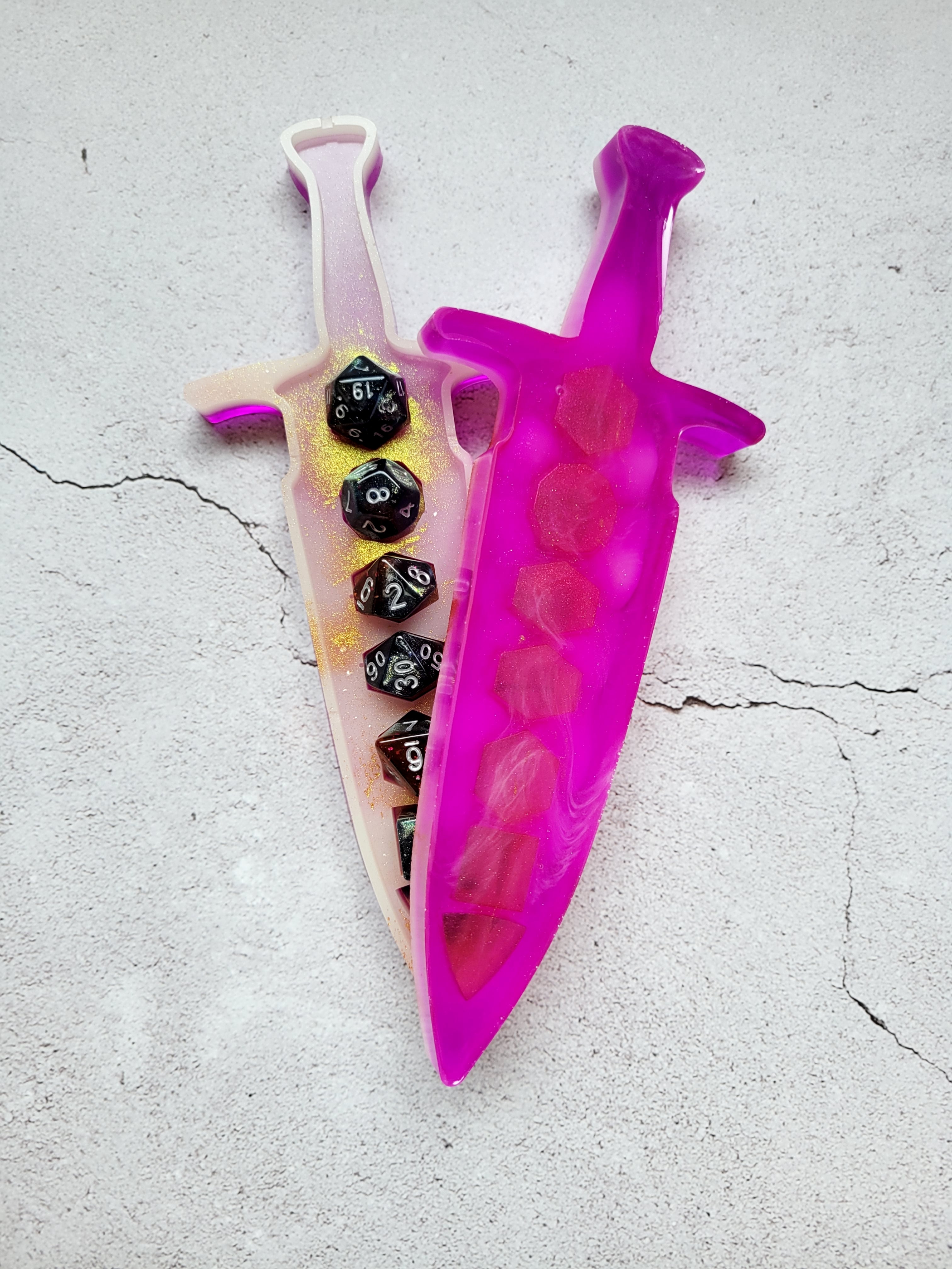 resin dice dagger holding a set of dice, open slightly. It's outside is bright pink, the inside is white with gold spray. Top view