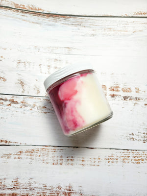 12oz burgundy marbled candle in a glass jar with a white lid laying on its side to show the colored swirls in the white wax. Candle name is Gingered Peach 