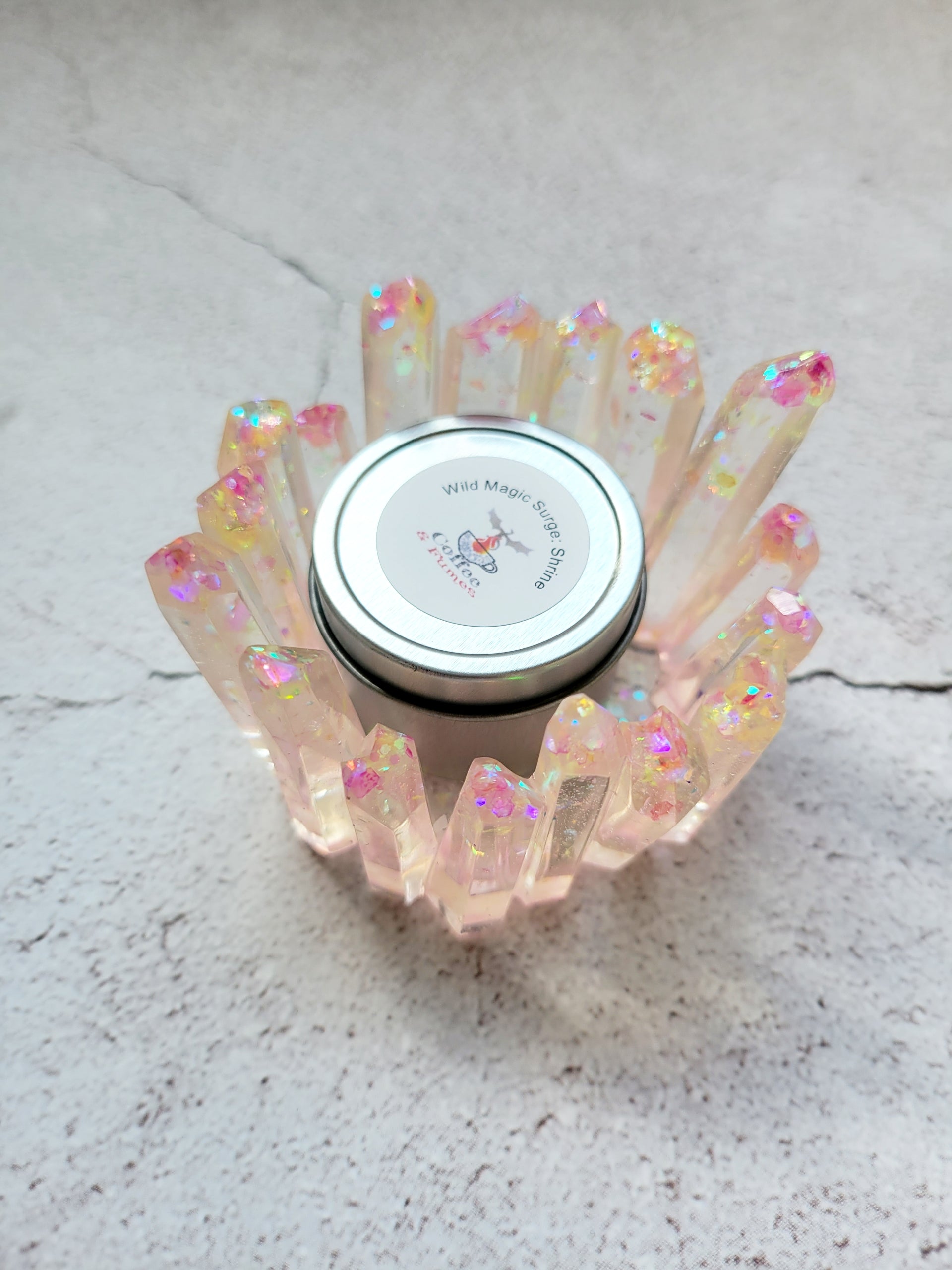 A side birds eye view of a tealight candle holder in the style of a cluster of crystals forming a circle. It's translucent clear with pink and yellow glitter. The crystals are various heights. There is a tealight candle inside to show size comparison.