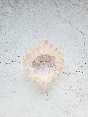 A birds eye view of a tealight candle holder in the style of a cluster of crystals forming a circle. It's translucent clear with pink and yellow glitter. The crystals are various heights.