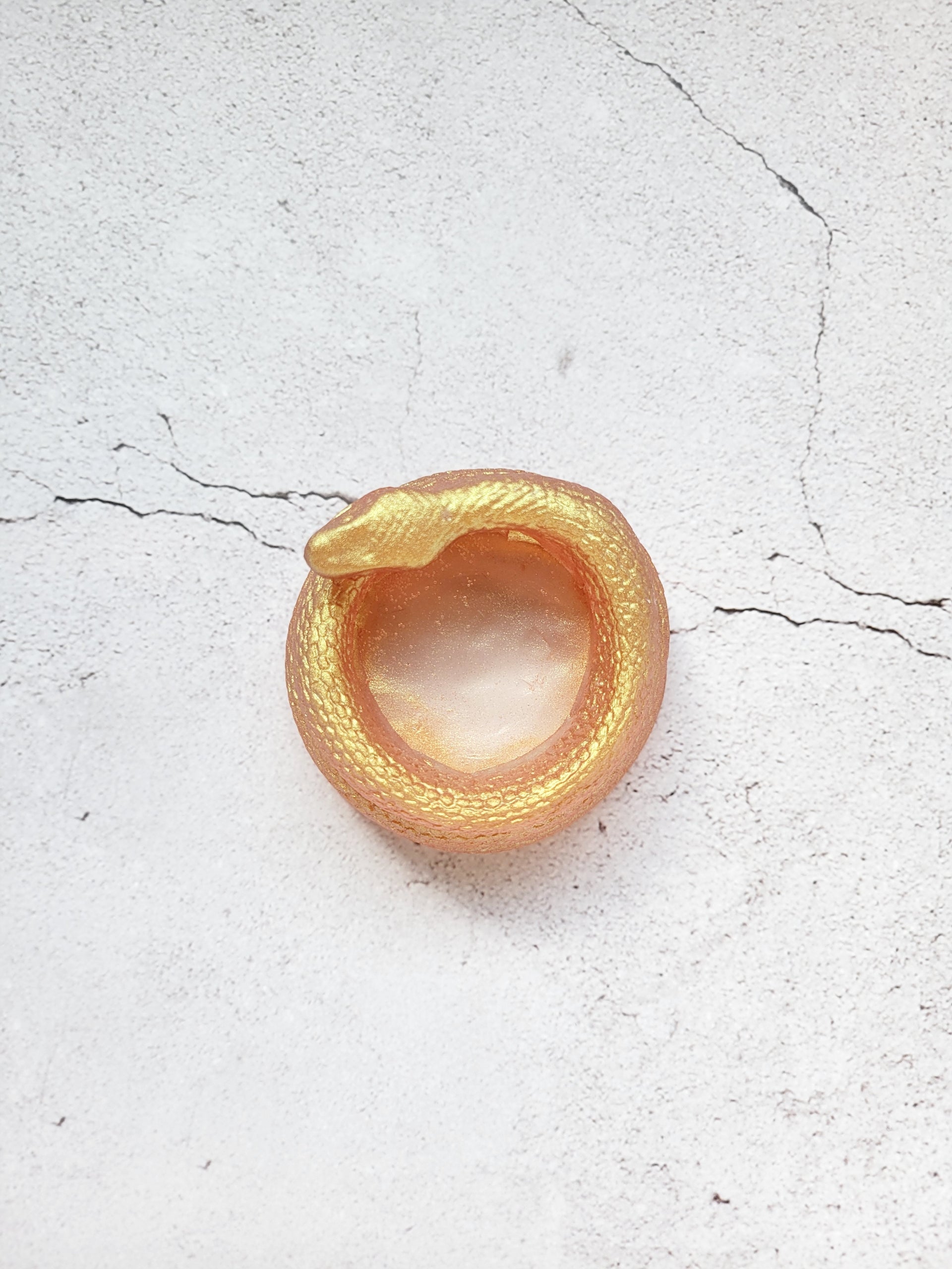 A top view of a tealight candle holder in the style of a coiled snake. It's a shimmering gold color.
