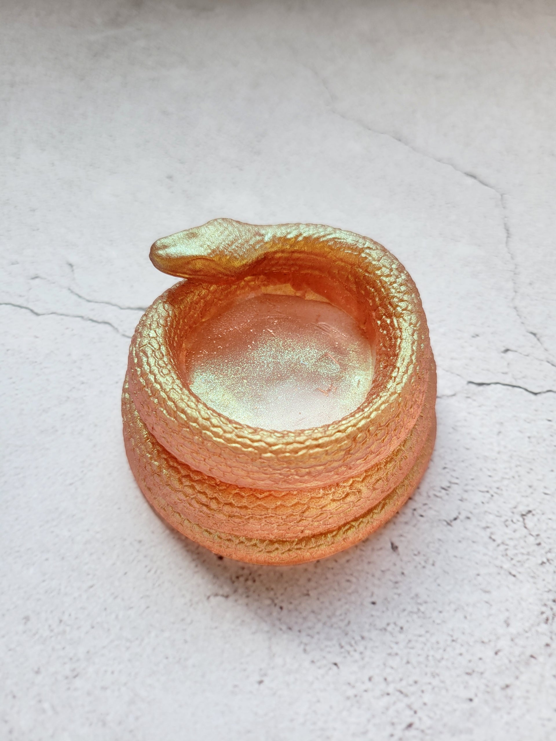 A side view of a tealight candle holder in the style of a coiled snake. It's a shimmering gold color.
