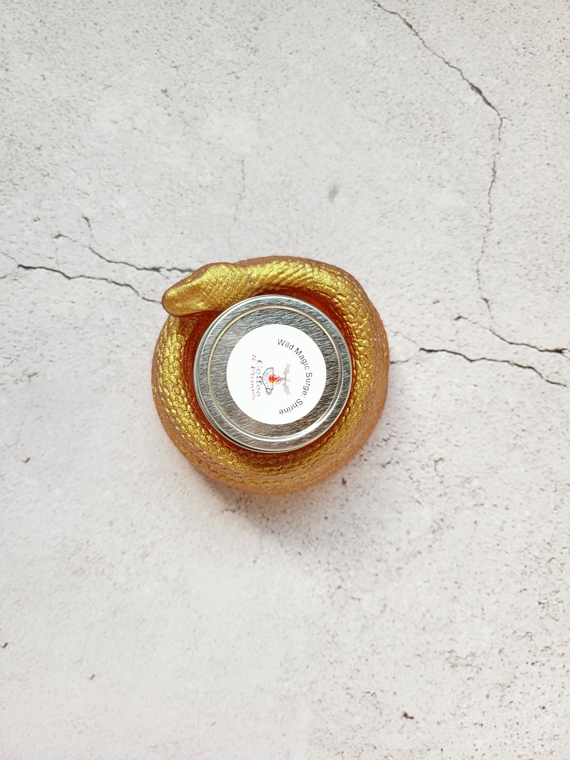 A top view of a tealight candle holder in the style of a coiled snake. It's a shimmering gold color. It has a tealight candle inside to show size comparison.