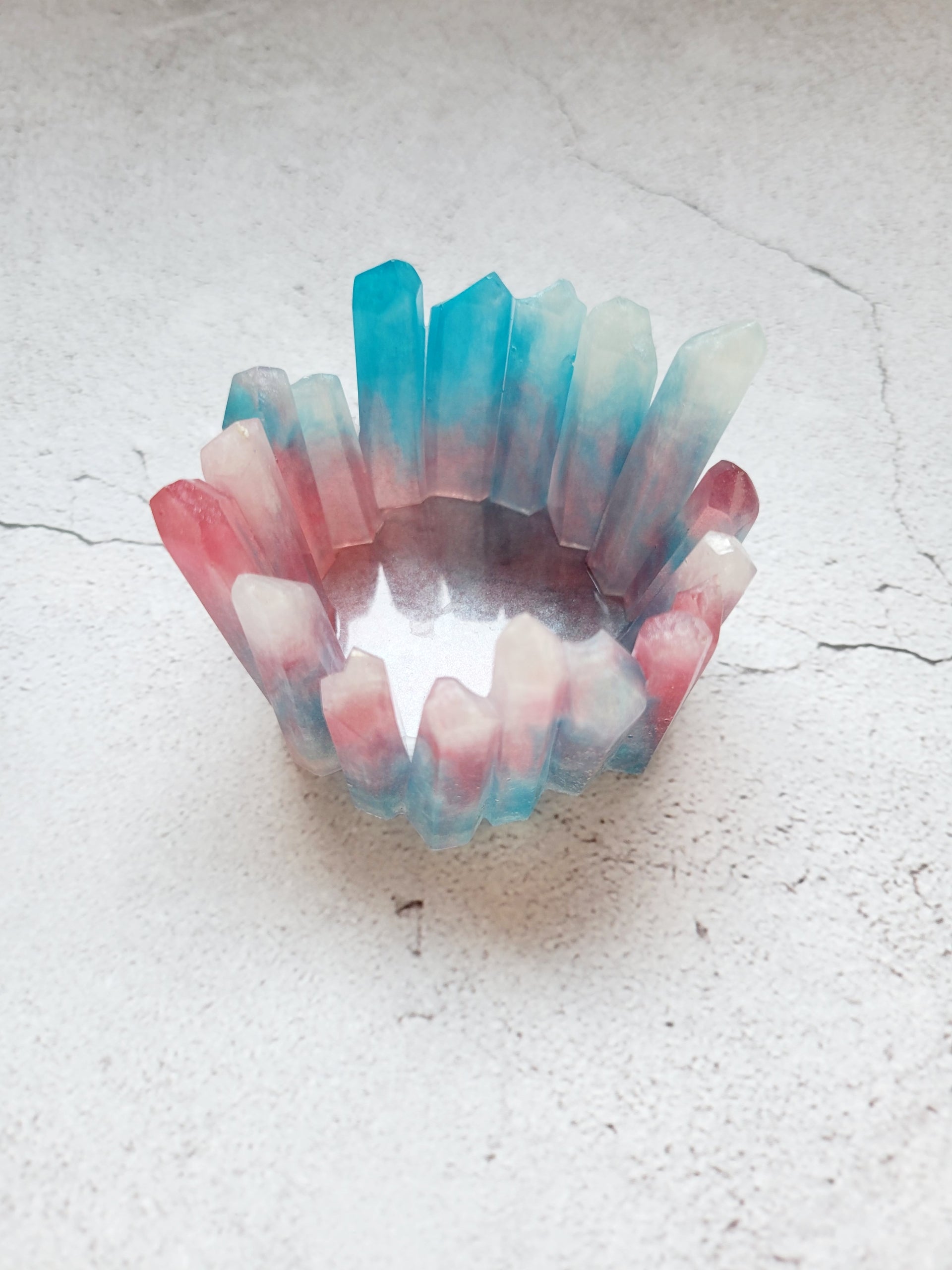 A side view of a tealight candle holder in the style of crystals in various heights. It's a mix of white, blue, pinks. 
