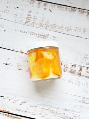 A 12oz marbled candle laying on its side to show the orange and yellow swirls in the wax. It has a white lid and glass jar. This candle is called Wild Magic Surge: Campfire. It's scent profile is smoke, sandalwood, pine. It has a mystery Dungeons and Dragons die inside.
