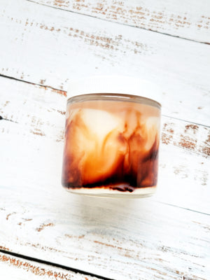 A 12oz marbled candle laying on its side to show the brown swirls in the wax. It has a white lid and glass jar. This candle is called Timeless: Carol's Candy Bar. It's scent profile is chocolate, caramel, marshmallow. 