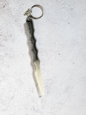 A black body and white tip defense keychain with finger grips on the middle. It has a silver chain and hoop.