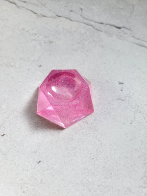 A side birds eye view of a pink and glittery hexagonal stand with a rounded dip in the center for holding dice or ball.