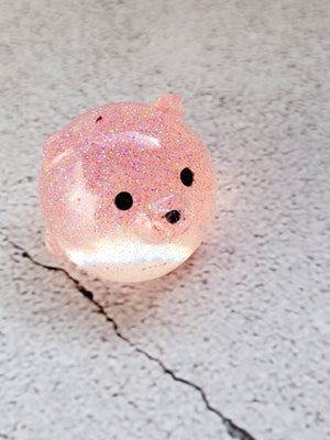A small round bear figure with black painted eyes and nose. It's a translucent pink with fine pink glitter.