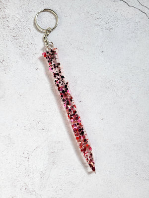 A defense keychain with silver chain and ring hoop. It's clear with pink and red glitter of various sizes. 