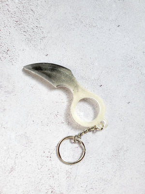 A defense keychain with a curved edge. It has a silver chain and hoop ring. It's white and black.