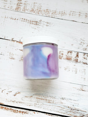 A side view of a 12oz marbled candle to show the blue and purple swirls.  It's in a glass jar with a white lid. This candle is called Critical Role: Jester's Spiritual Weapon. It's scent profile is cotton candy, vanilla, red wine. It has a mystery Dungeons and Dragons die inside.