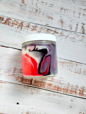 A side view of a 12oz marbled candle to show the black and red swirls in the wax. It's in a glass jar with a white lid. This candle is called Star Wars: Mustafar. It's scent profile is smoke, peppercorn, musk.