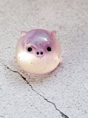 A small round pig figure with black painted eyes and nose. It's clear with a purple pink head.