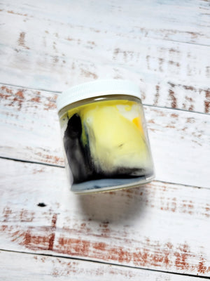 A side view of a 12oz marbled candle to show the yellow and black swirls in the wax. It's in a glass jar with a white lid. This candle is called Timeless: Lucy's Journal. It's scent profile is leather, tobacco, musk. 