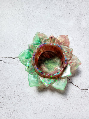 A birds eye view of a tealight candle holder in the style of a lotus flower. It's got green and brown coloring with flecks of colorful glitter along the petals. 