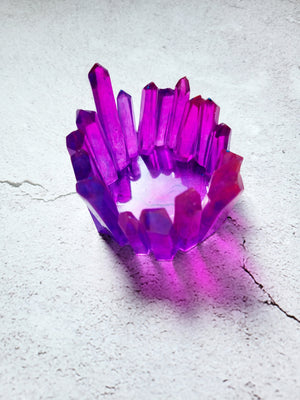 A side birds eye view of a tealight candle holder in the style of crystals forming a circle. The crystals are varying heights. They are a translucent purple red color.