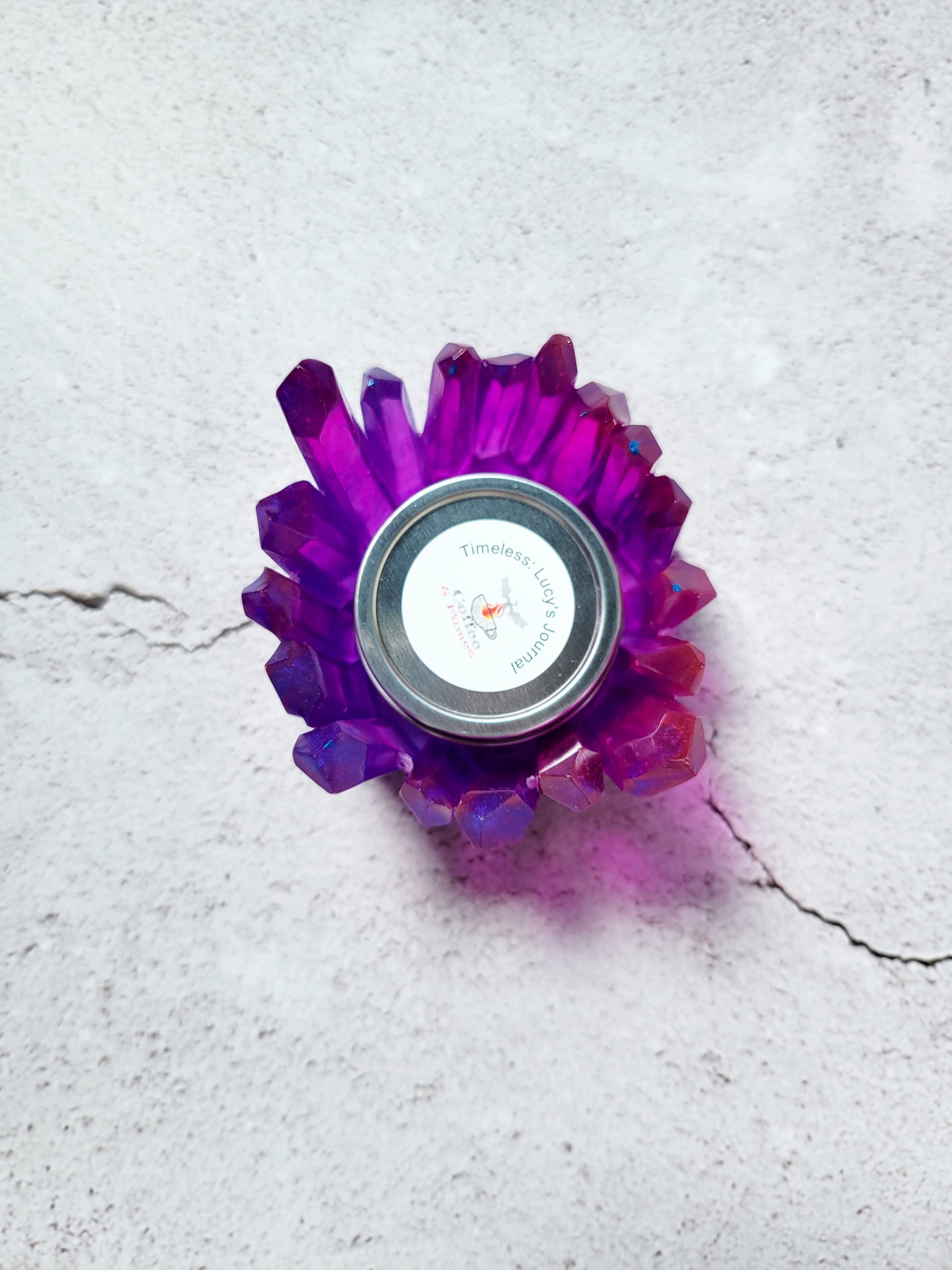 A birds eye view of a tealight candle holder in the style of crystals forming a circle. The crystals are varying heights. They are a translucent purple red color. There is a tealight candle inside to show size comparison.
