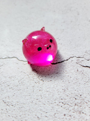 A small round pig figure with black painted eyes and nose. It's bright translucent pink.