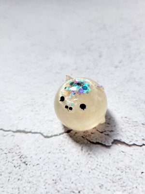 A small round pig figure with black painted eyes and nose. It's white with colorful glitter on the top of its head.