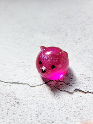 A small round bear figure with black painted eyes and nose. It's a deep pink color.