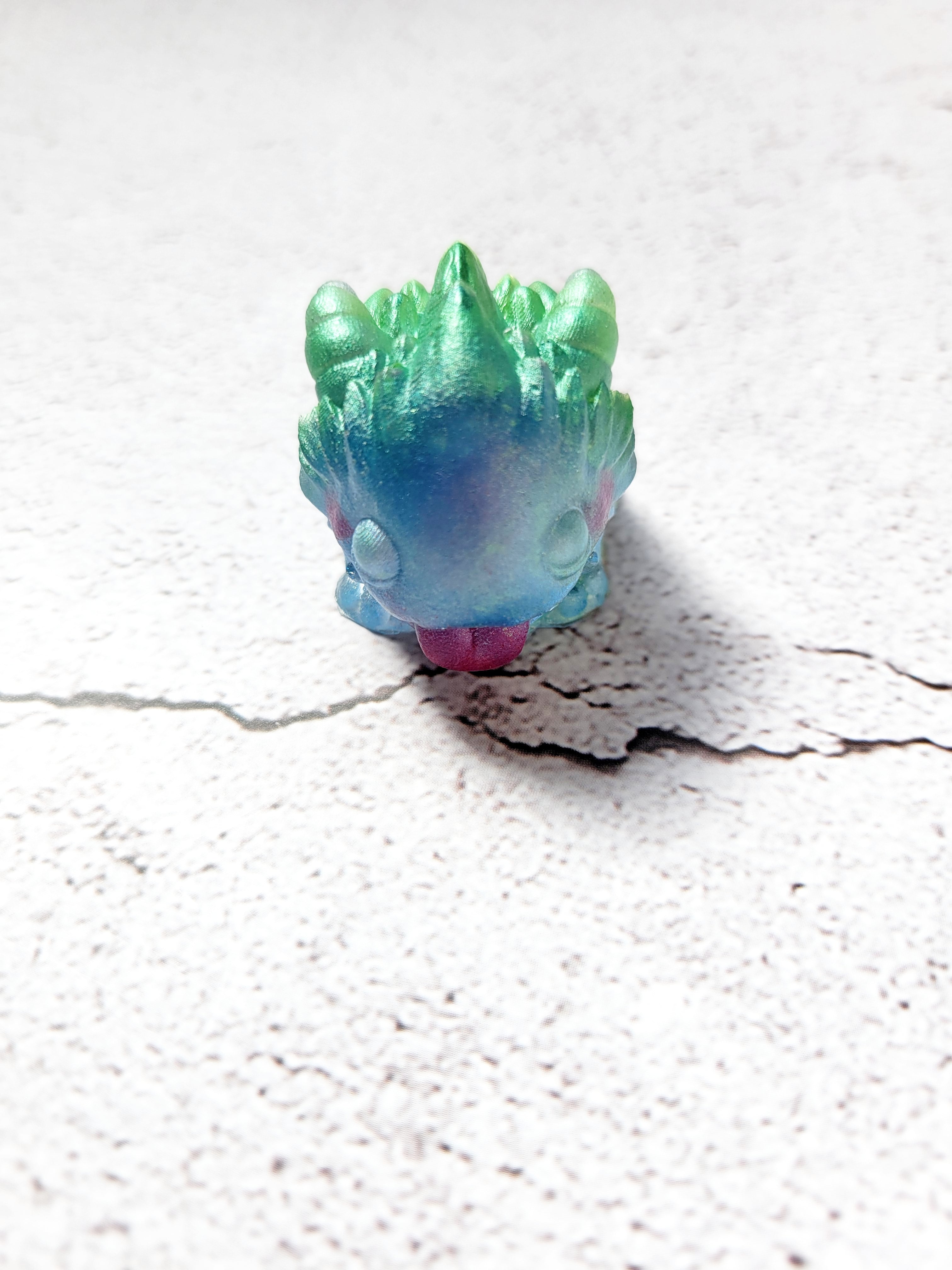 A front view of a spiked monster figure. The body is blue, spikes green, tongue red with red cheeks.