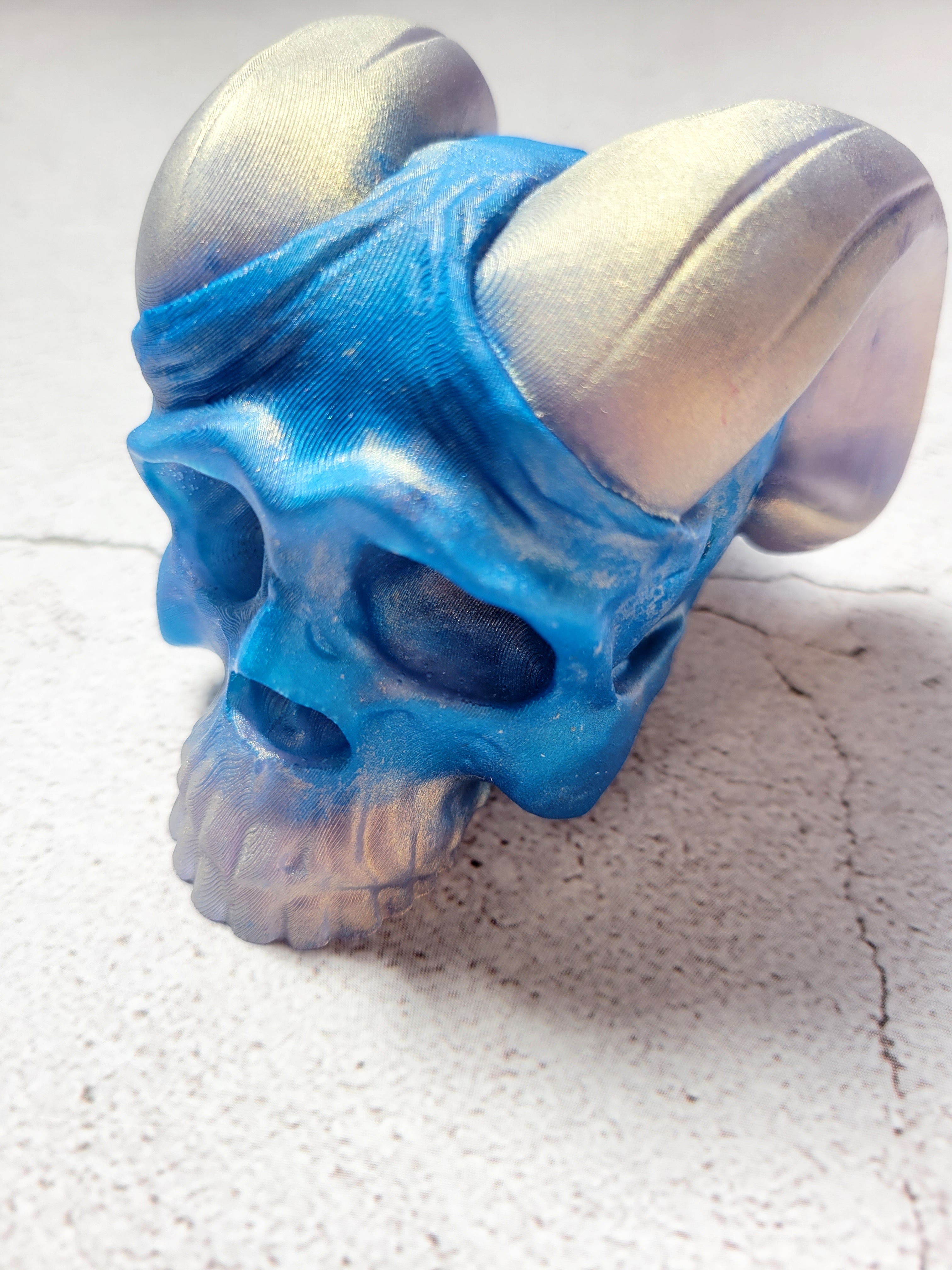 A front view of a skull with curved horns. it's teeth and horns are silver. The skull is blue.