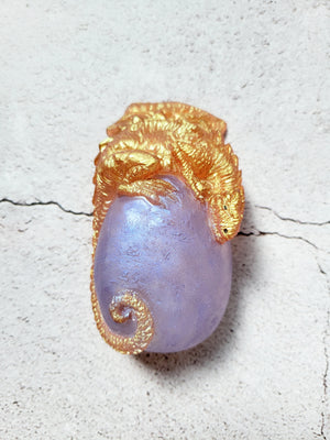 A dragon and egg figure. The dragon is gold with black eyes and nostrils. It's perched on the top of a lavender egg, its tail wrapping near the bottom.