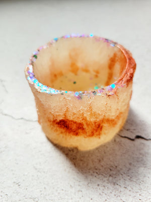 A tealight candle holder that has the texture of tree bark, its round, white and brown with blue, green, purple glitter around the opening.