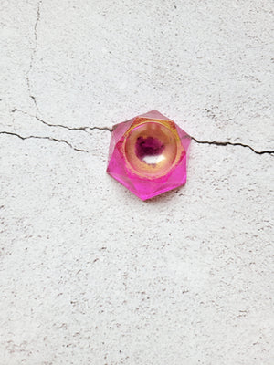 A top view of a hexagonal stand to hold a die or tabletop familiar. It's pink and gold with a black center to mimic an eye.