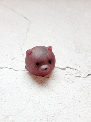 A small round bear figure with black painted eyes and nose. It's a matte finish. It's a red wine color. 