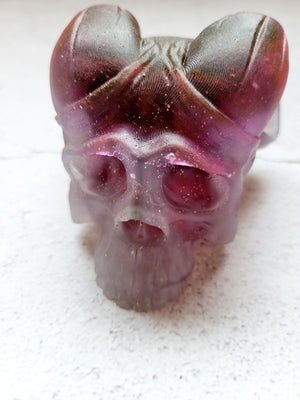 A front view of a skull with curved horns. It's a pale to dark purple in color. 