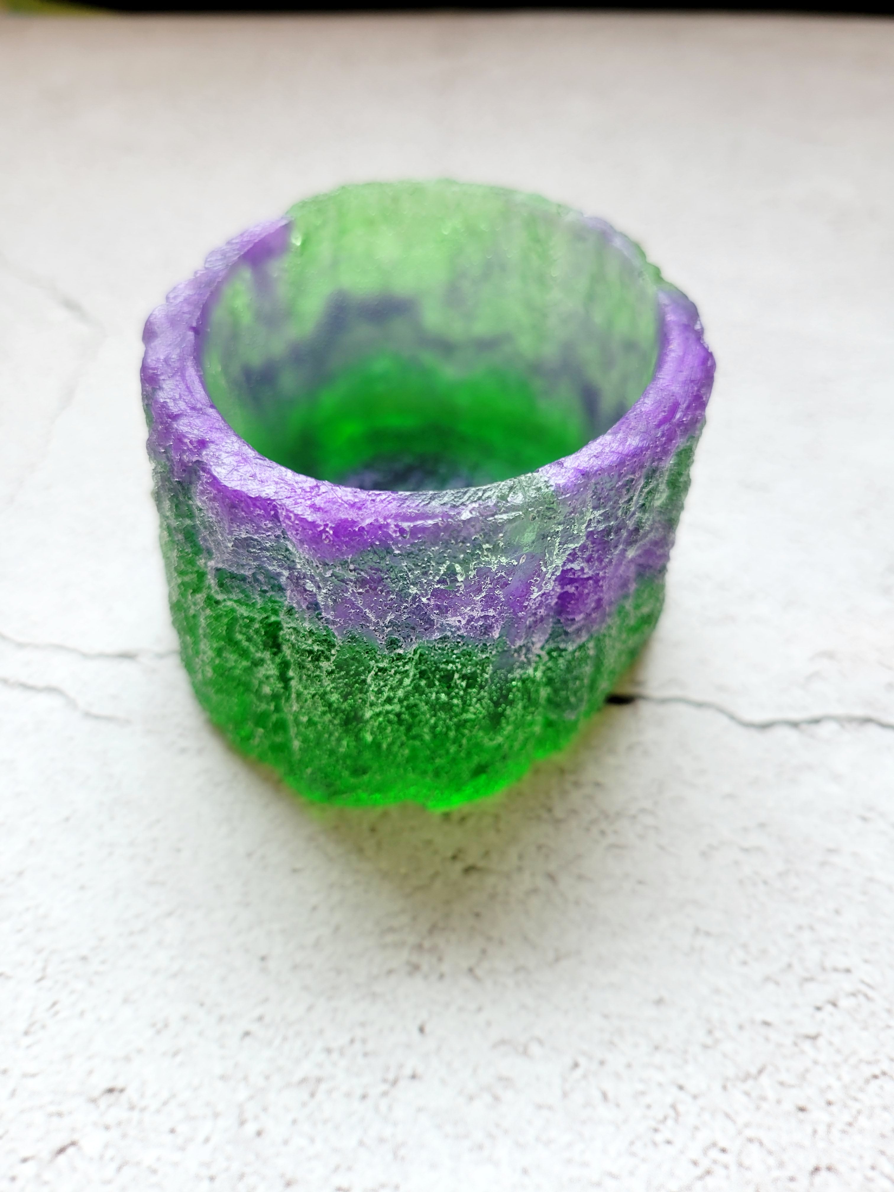 A side view of a tealight candle holder in the style of a tree trunk. It's texture to feel like bark. It's purple and green.