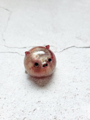 A small round pig figure with black painted eyes and nose. It's a shimmery red and gold color.