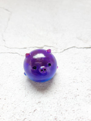 A small round pig figure with black painted eyes and nose. It's a blue/purple combination.