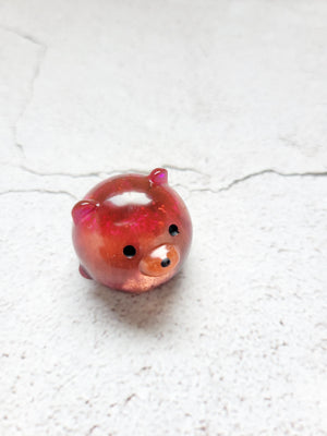 A small round bear figure with black painted eyes and nose. It's a mixture of red, orange, and pink coloring. 