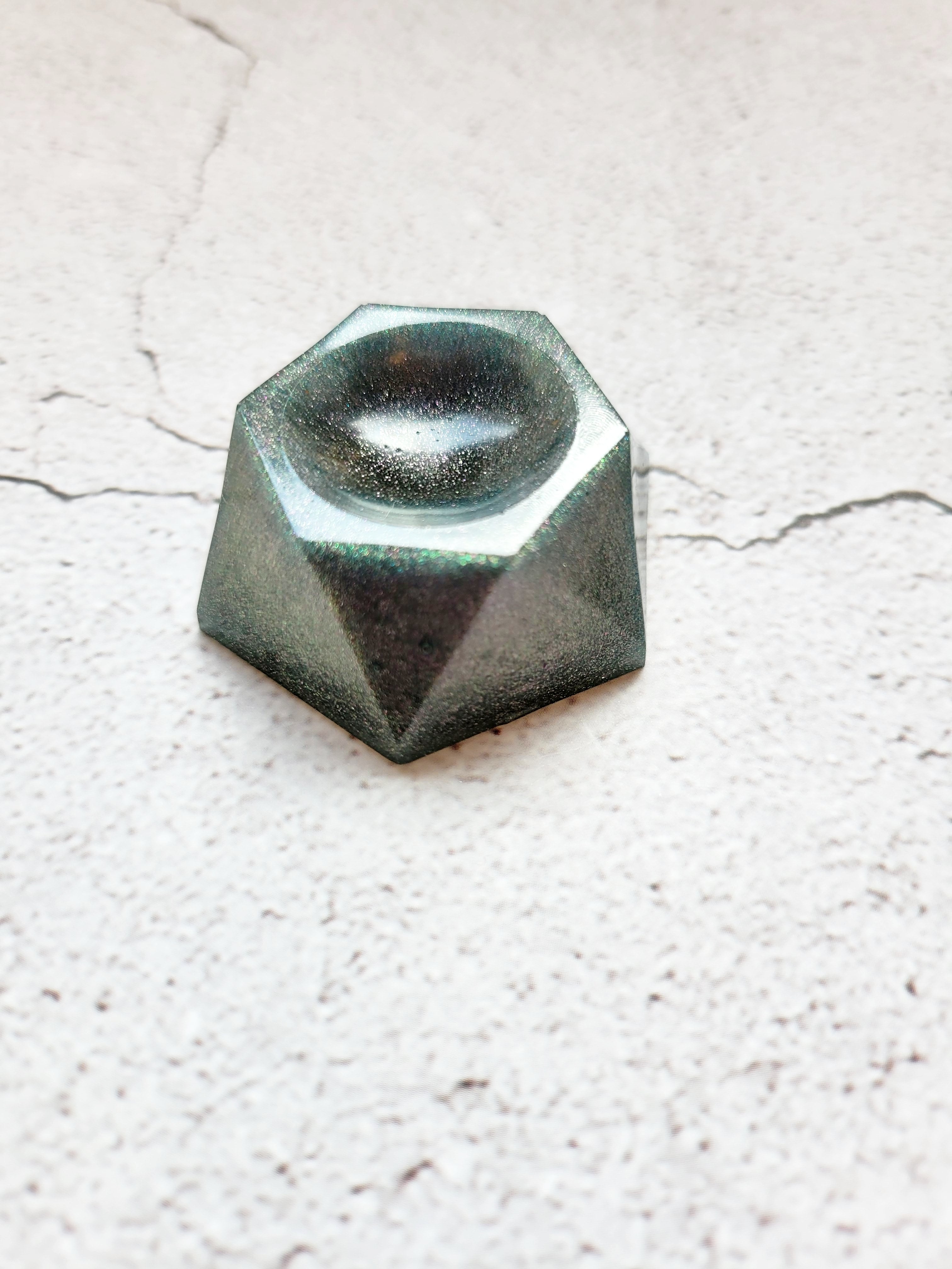 A side view of a hexagonal stand for dice or tabletop familiar. It's pale gray with sparks of color.