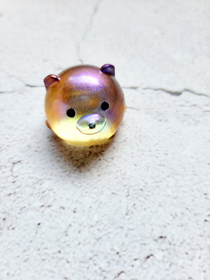 A small bear figure with black painted eyes and nose. It's got color shifting pigments, showing pinks, oranges, yellows.
