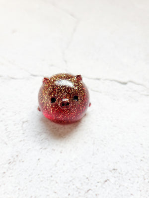 A small round pig figure with black painted eyes and nose. It's red with fine gold glitter throughout.