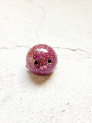A small round penguin figure with black painted eyes. It's a plum color with fine gold glitter throughout. 