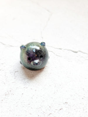 A small round bear figure with black eyes and nose. It's color shifting with hints of green, blues, purples and fine glitter mixed throughout.